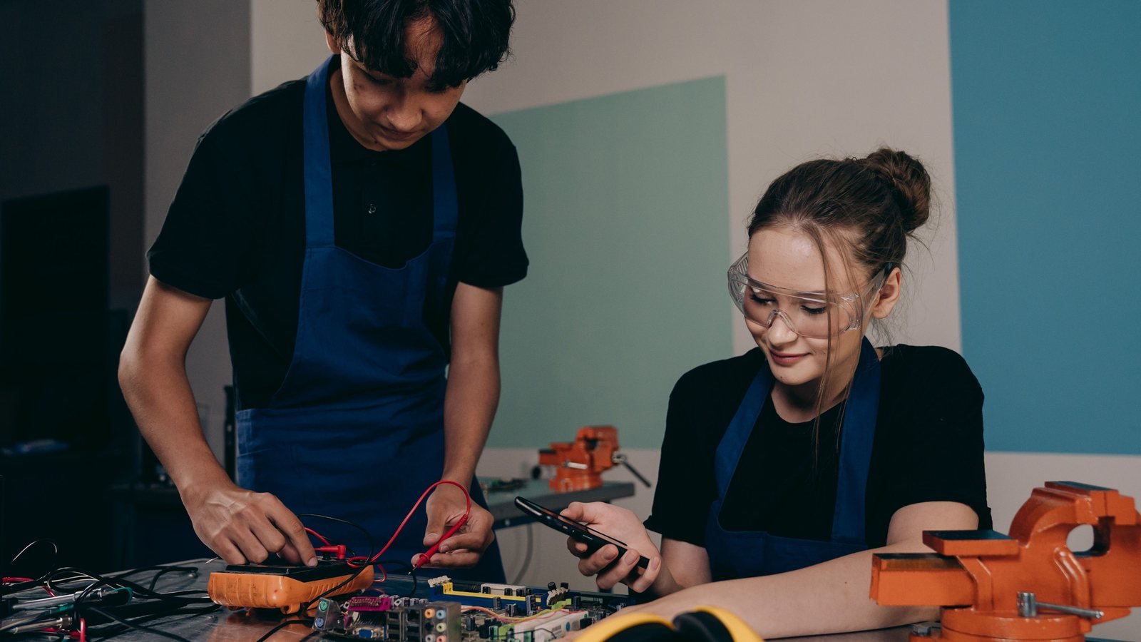 Two people practicing electronics work together at a workbench.