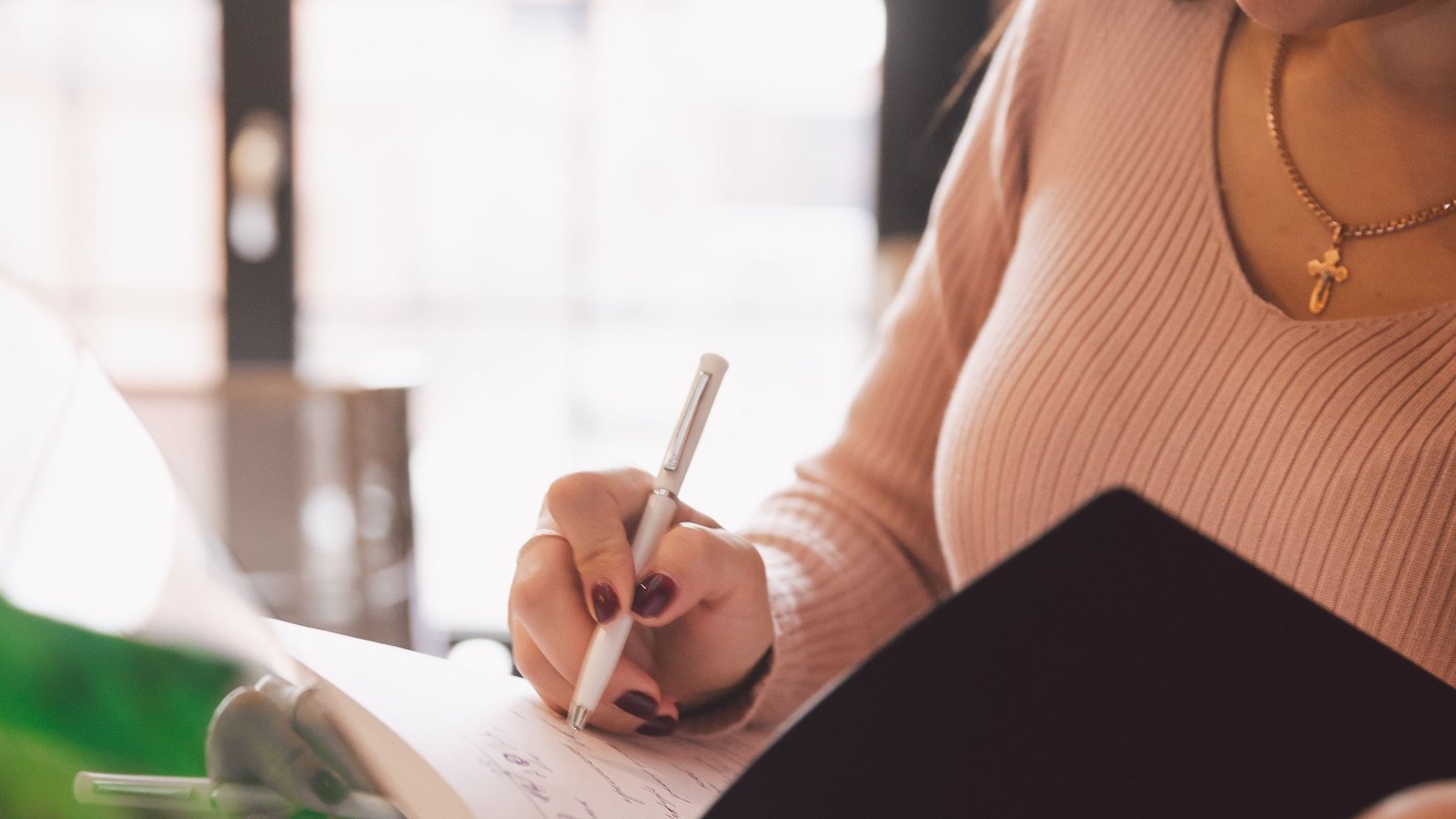 Young adult writing notes beside a laptop while preparing application material.